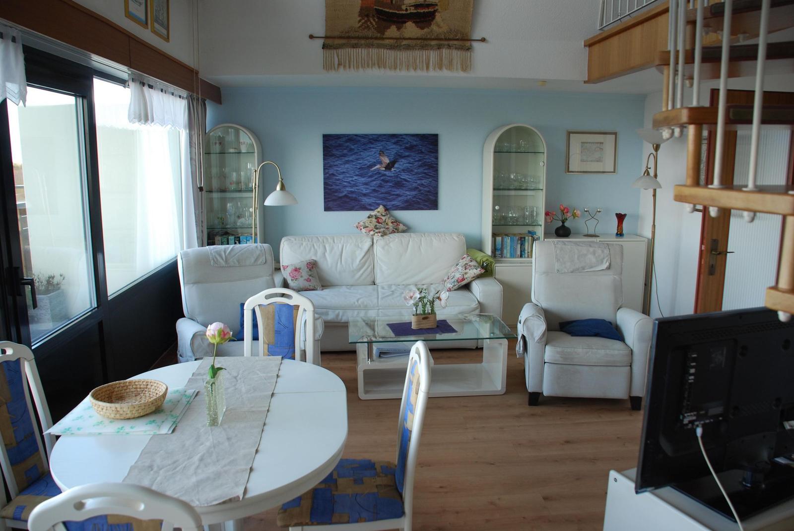 Wohn- und Essbereich mit Sofa, Stühlen und Tisch. Glaswand und Treppenhaus sichtbar.