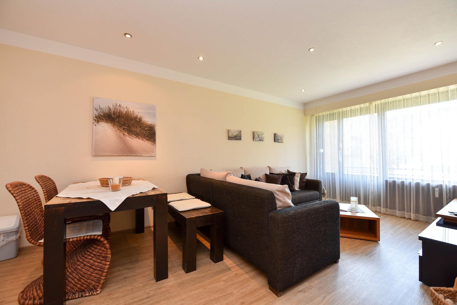 Wohn- und Essbereich mit Sofa, Tisch, Stühlen und Fenster mit Vorhängen.