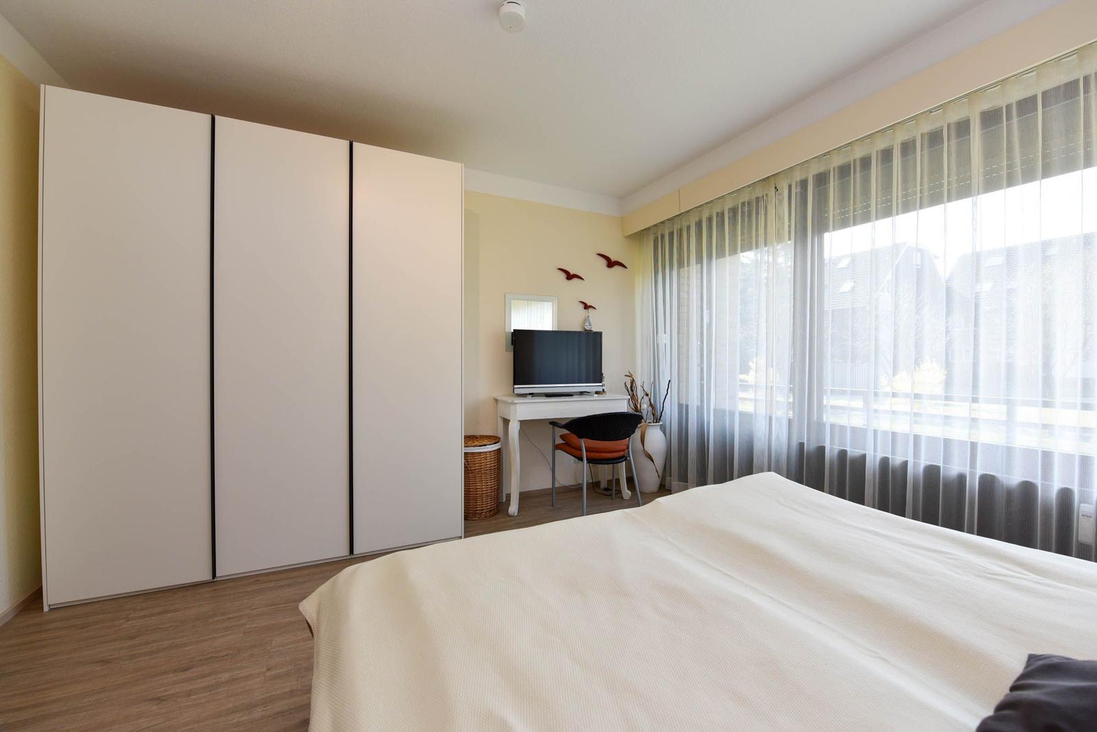 Schlafzimmer mit Bett, Kleiderschrank und Schreibtisch mit Fernseher.