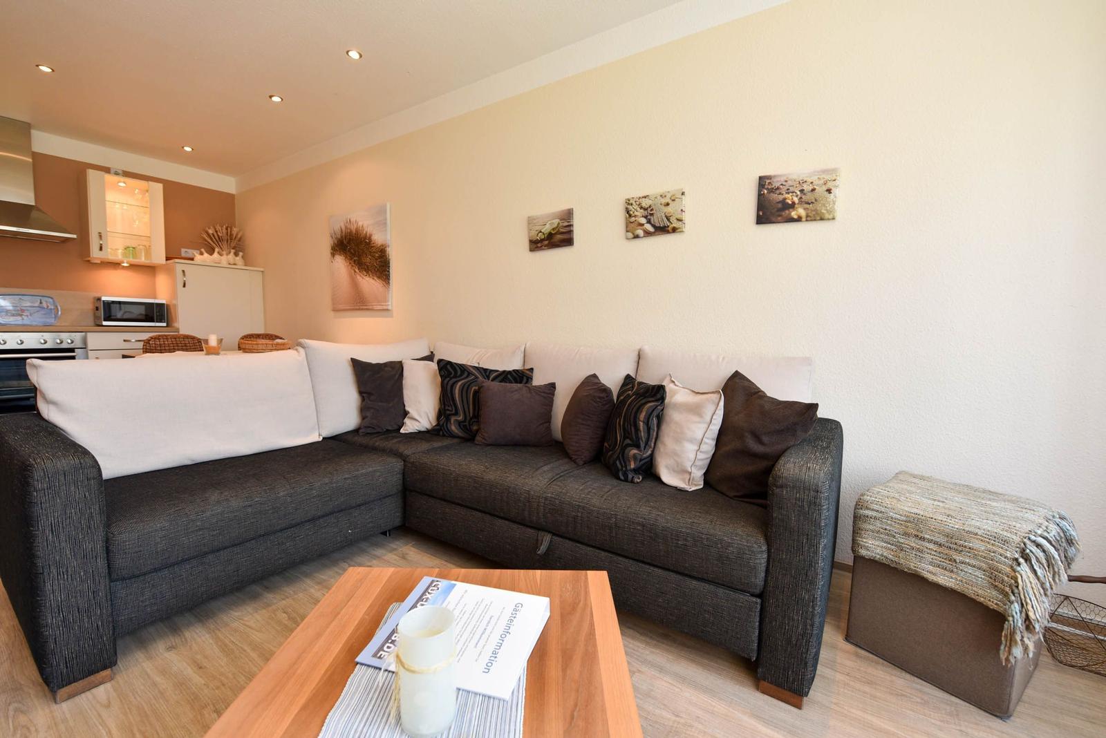 Wohnzimmer mit Ecksofa, Couchtisch und Küchenbereich im Hintergrund.