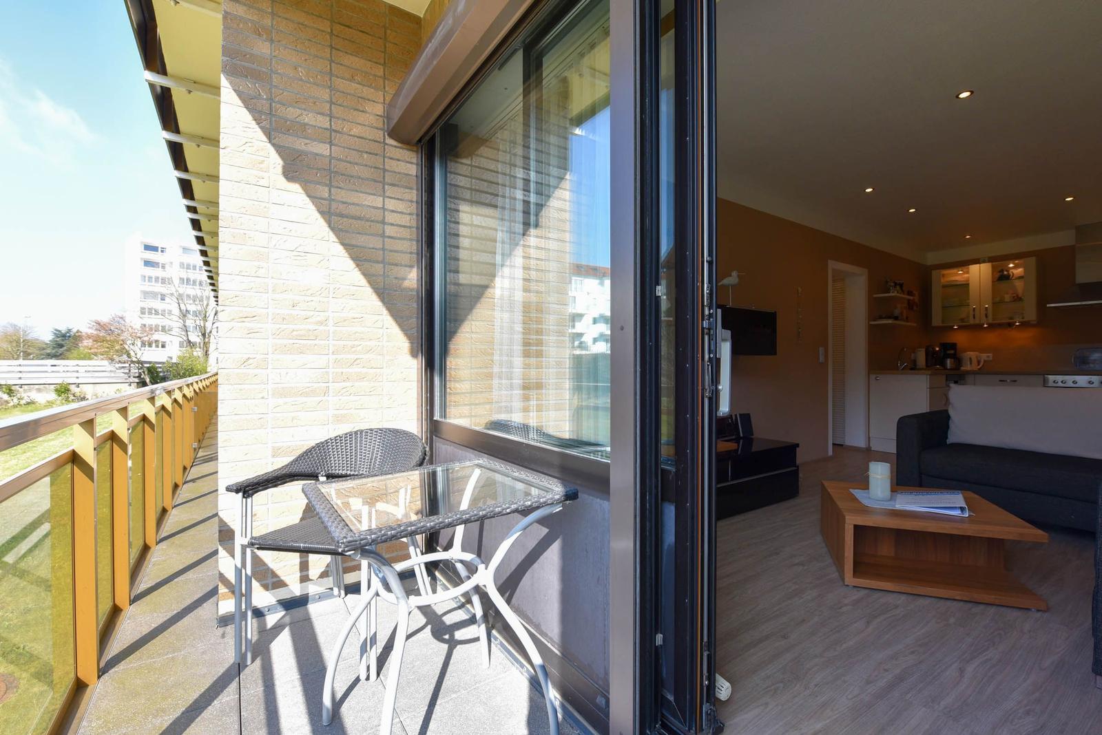 Balcony with table and chairs. Living room with sofa, coffee table, and kitchen visible.