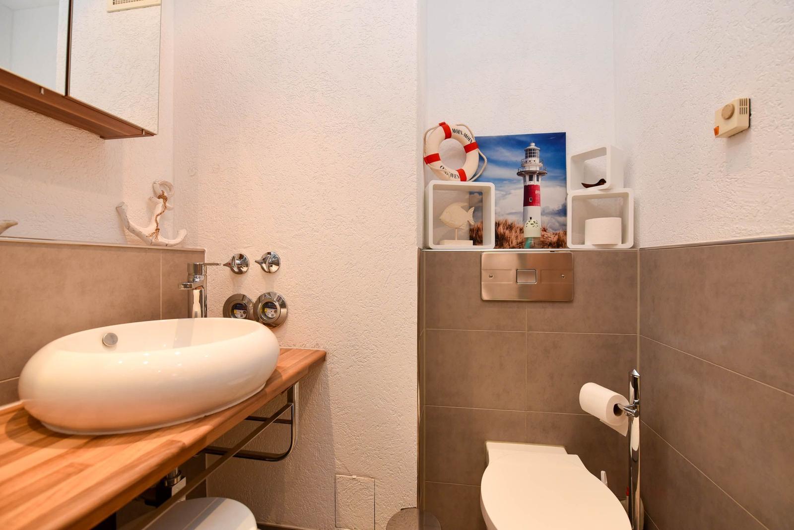 Badezimmer mit Waschbecken auf Holzunterlage, Toilette und maritimen Dekorationen.
