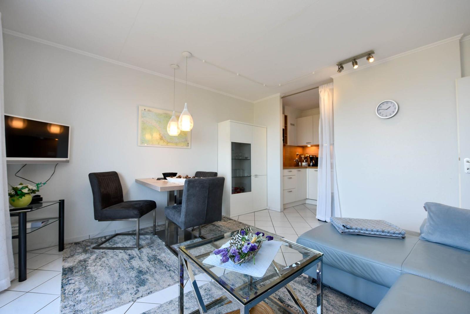 Wohnzimmer mit Sofa, Glas-Tisch und Essbereich. Küche ist angebaut.