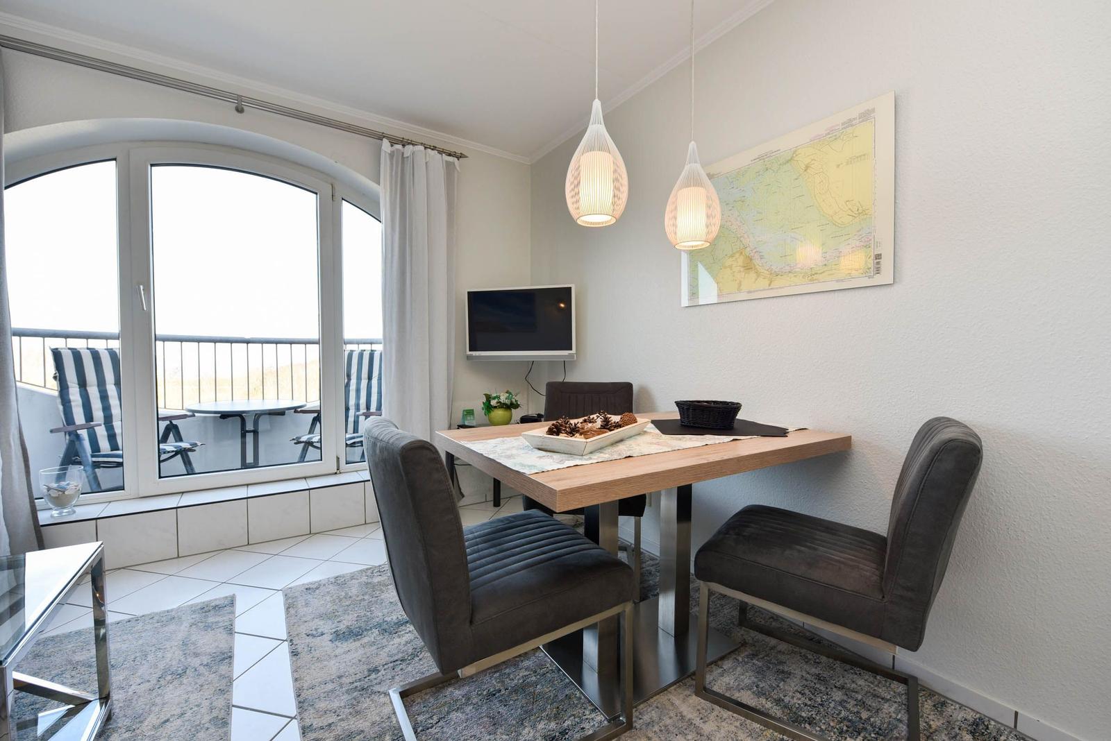 Essbereich mit Tisch, Stühlen und Balkonansicht. Wandbild und Deckenleuchten.