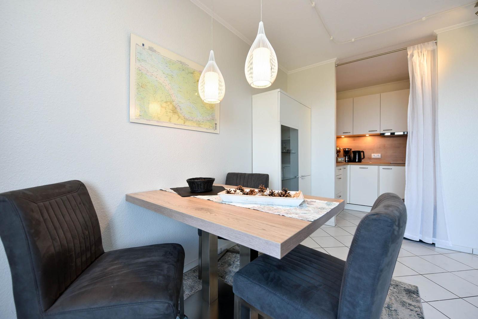 Essbereich mit Tisch, Stühlen und Karte an der Wand. Küche im Hintergrund.