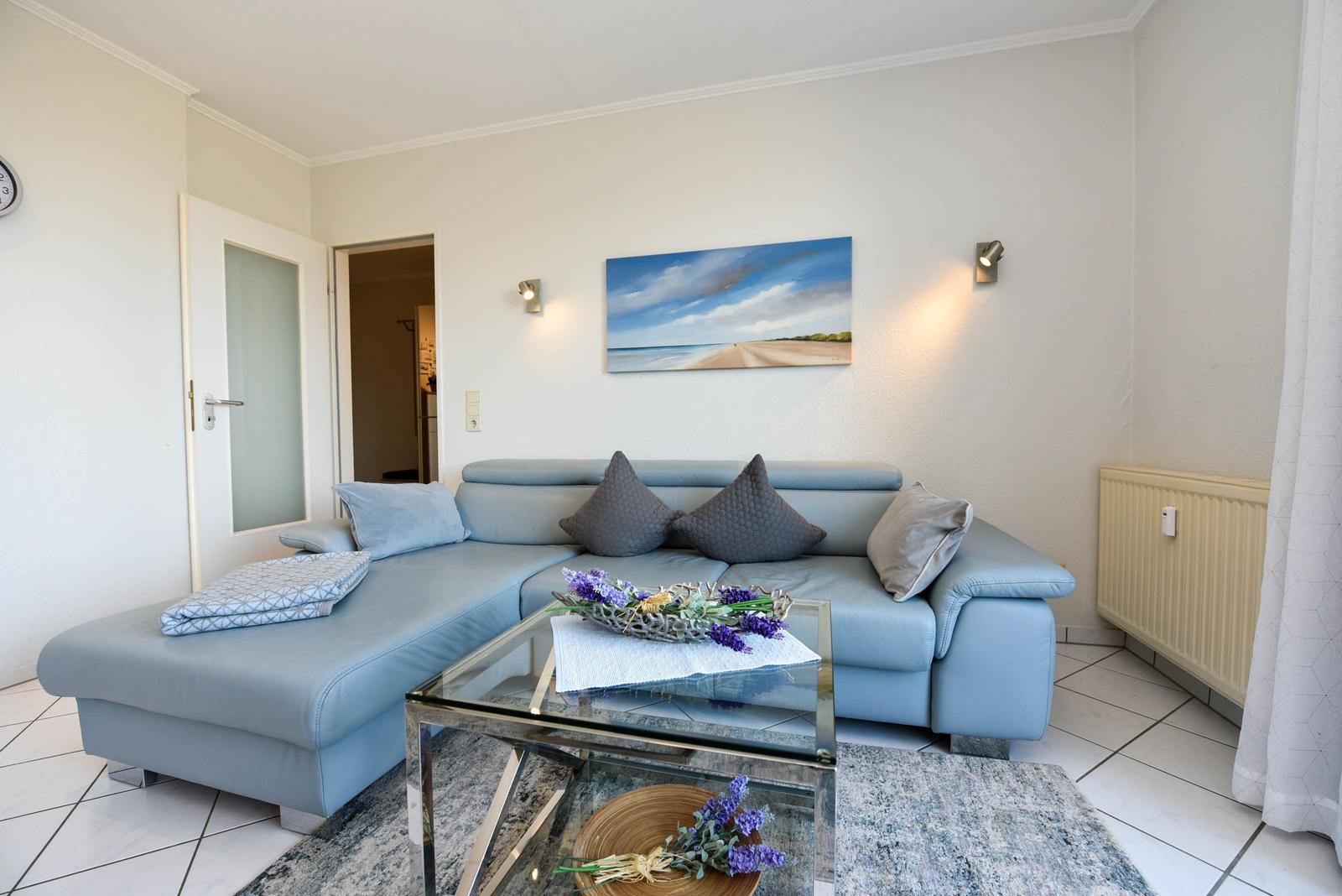 Ein Wohnzimmer mit blauem Sofa, Glas-Tisch und Wandbild an der Wand.