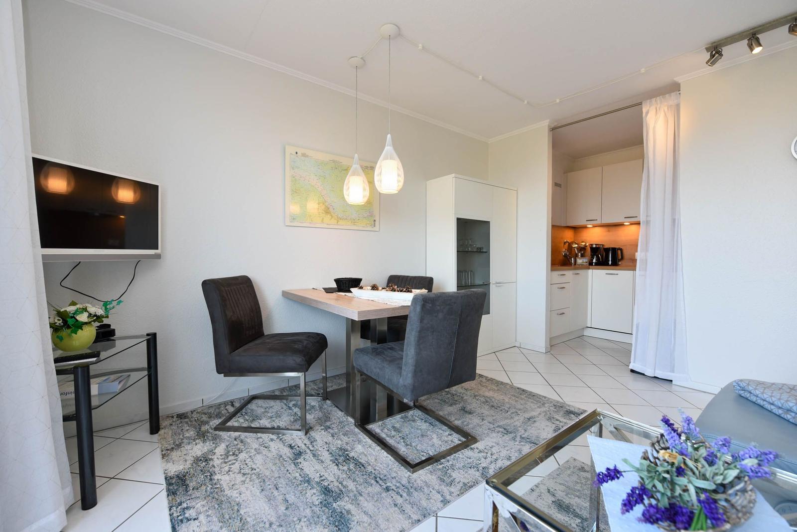Essbereich mit Tisch, Stühlen und TV. Küche im Hintergrund.