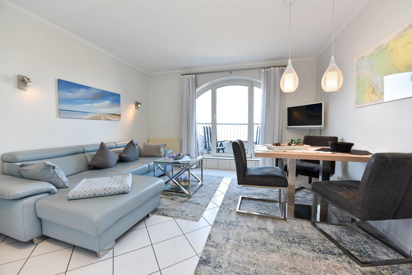 Wohn- und Essbereich mit Sofa, Esstisch und Balkonzugang.