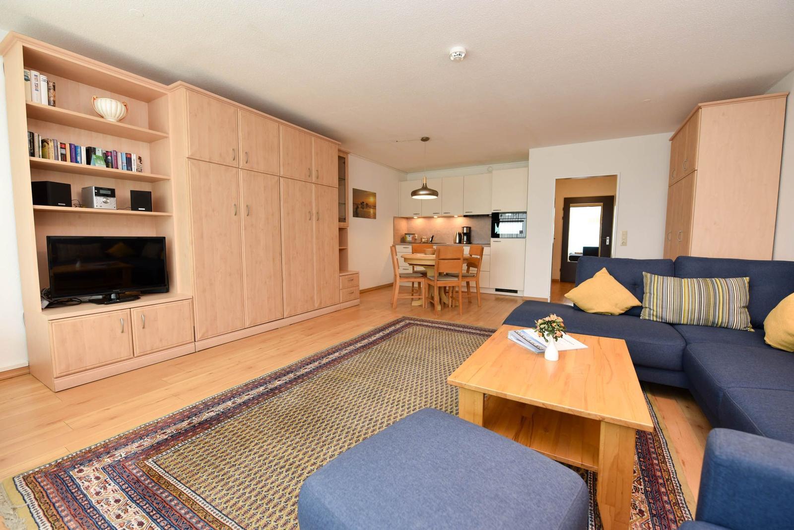 Wohnzimmer mit Sofa, Couchtisch und integriertem Schrank. Küche und Essbereich im Hintergrund.
