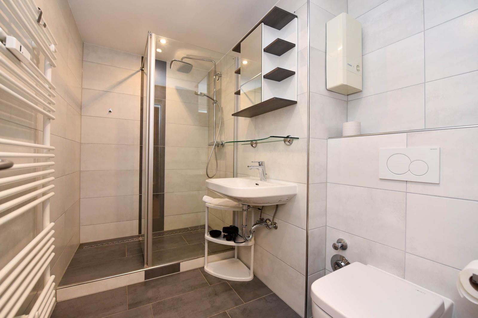 Badezimmer mit Dusche, Waschbecken und Toilette. Weiße Fliesen und modernes Design.
