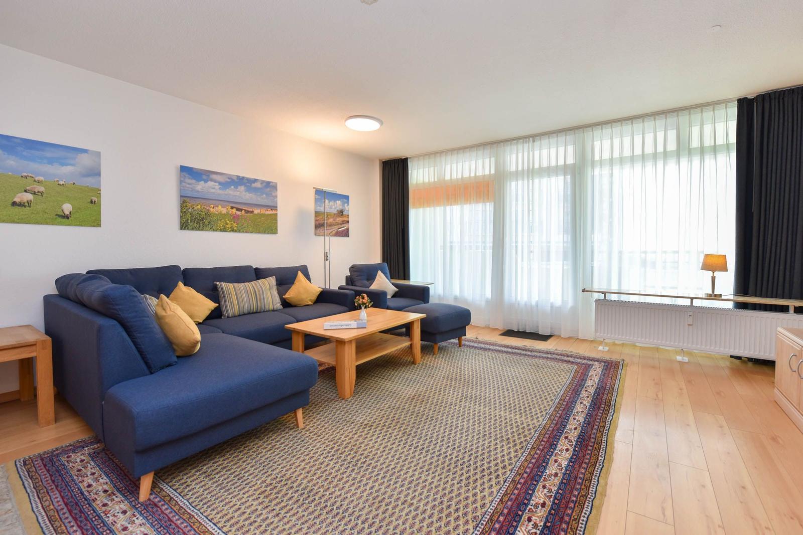 Ein Wohnzimmer mit blauem Sofa, Holztisch und großen Fenstern mit Vorhängen.