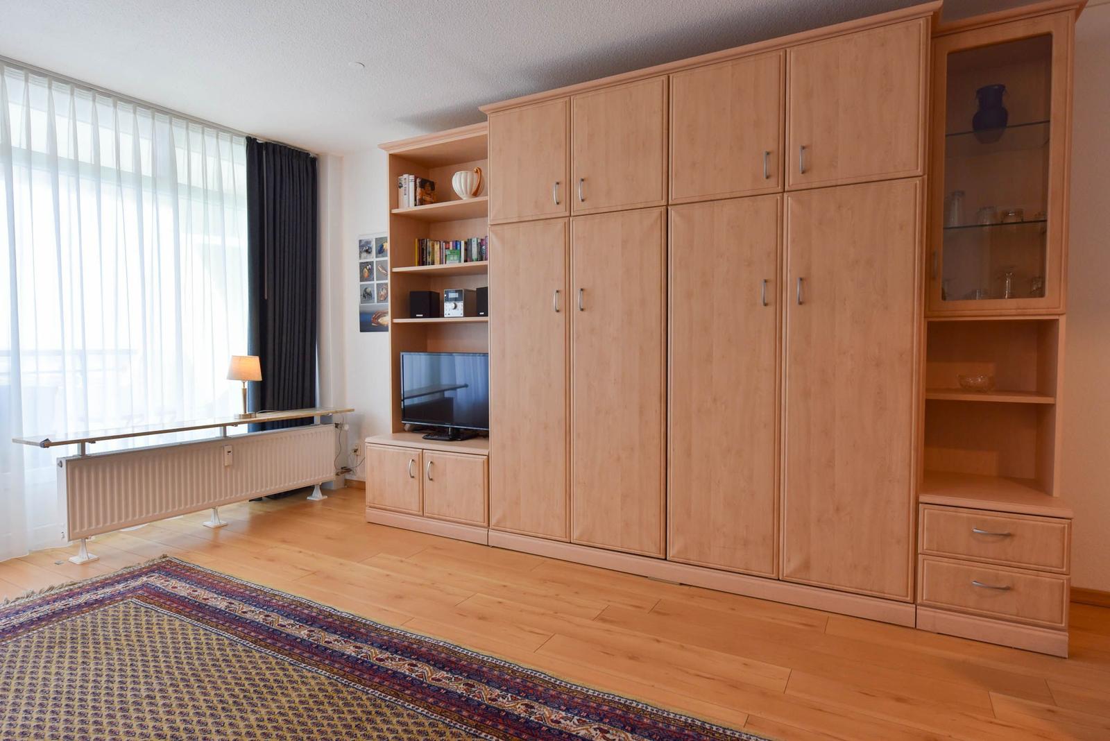 Großer Raum mit Holzmöbeln, TV, Fenster und Teppich.