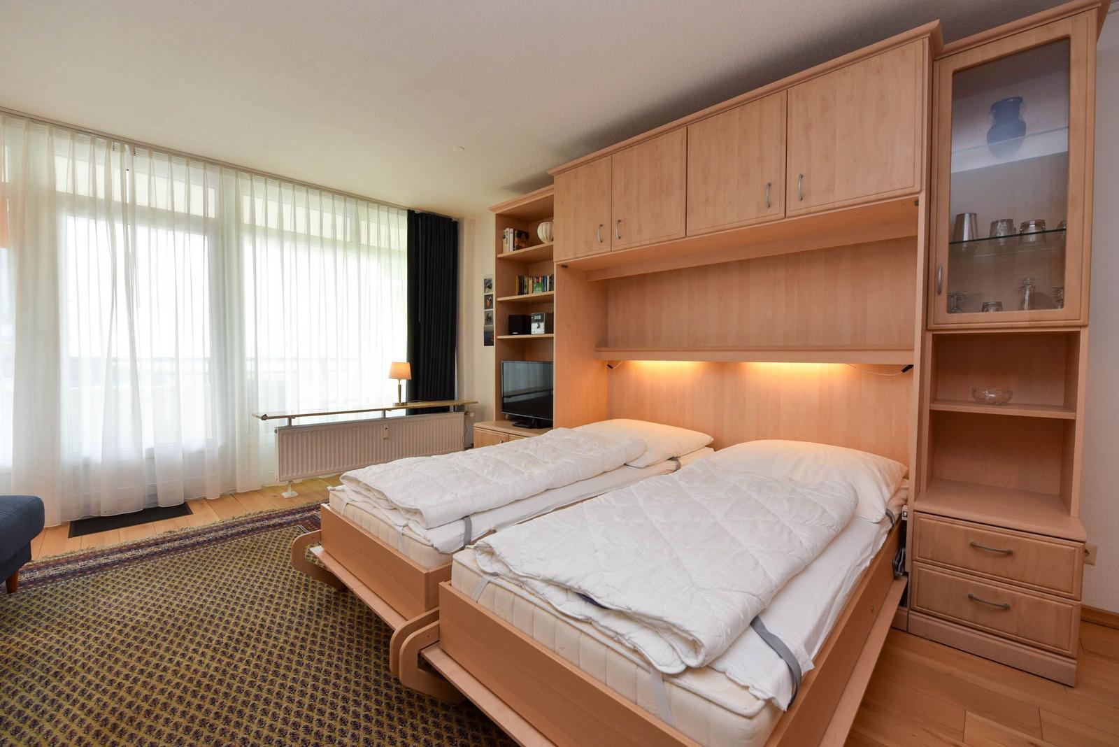 Zwei Einzelbetten unter einem Holzschrank mit Schubladen und Glasfronten.
