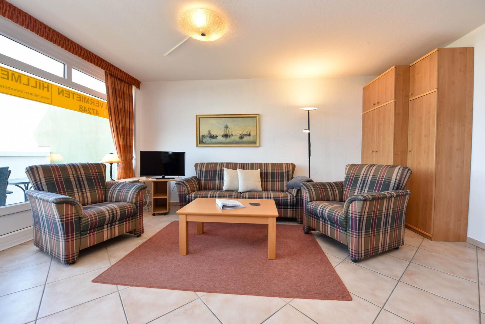 Wohnzimmer mit Plaid-Sofa, zwei Sesseln, Couchtisch und TV.