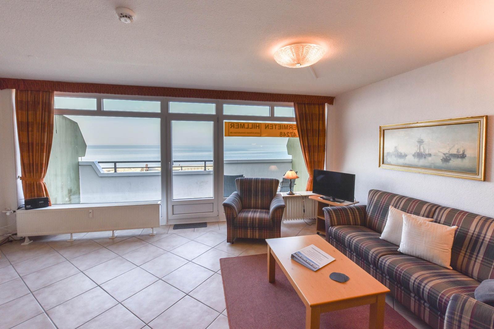 Wohnzimmer mit Sofa, Sessel und Blick aufs Meer durch Glastüren.