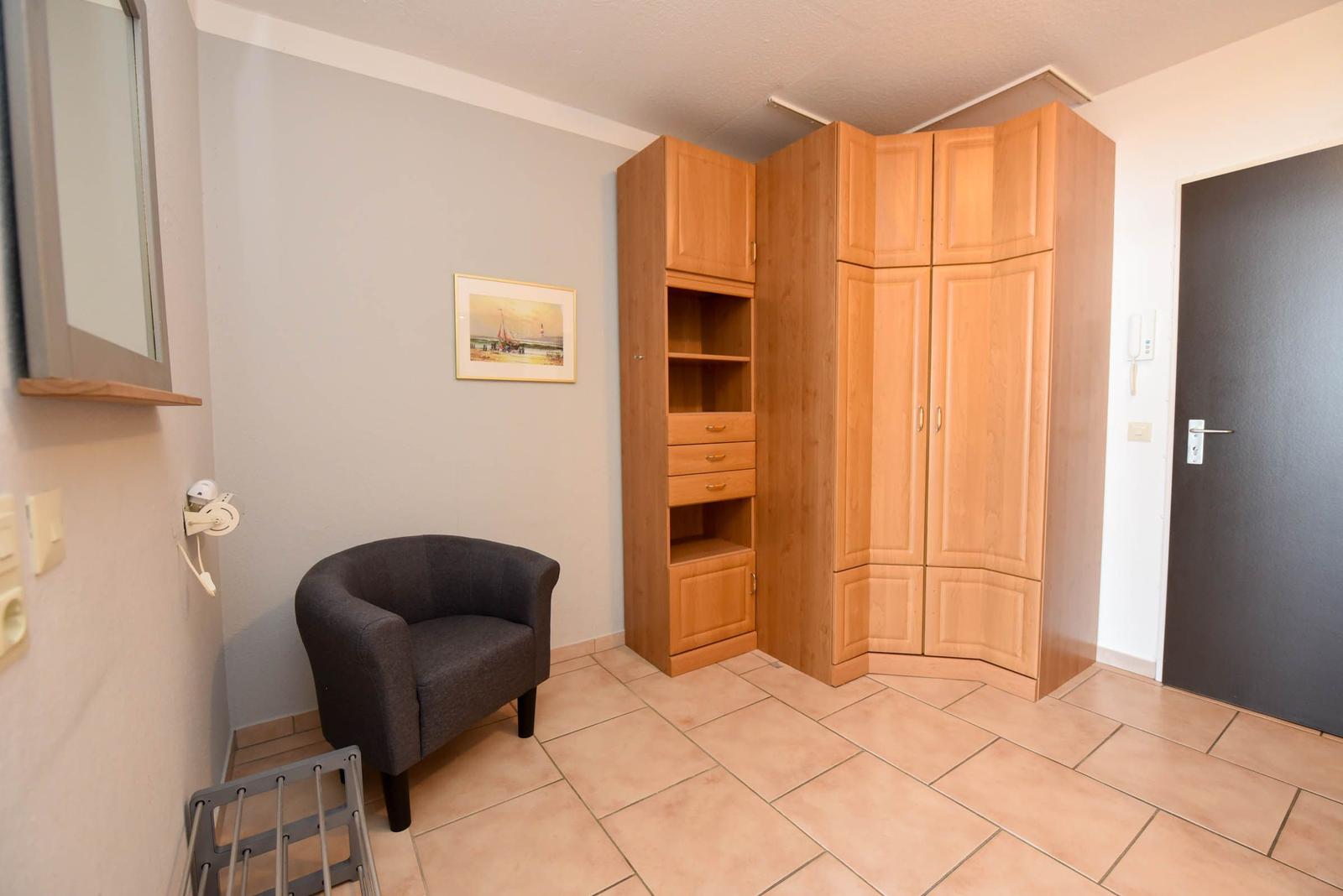 Ein Raum mit einem grauen Sessel, einem Holzschrank und einem Bild an der Wand.