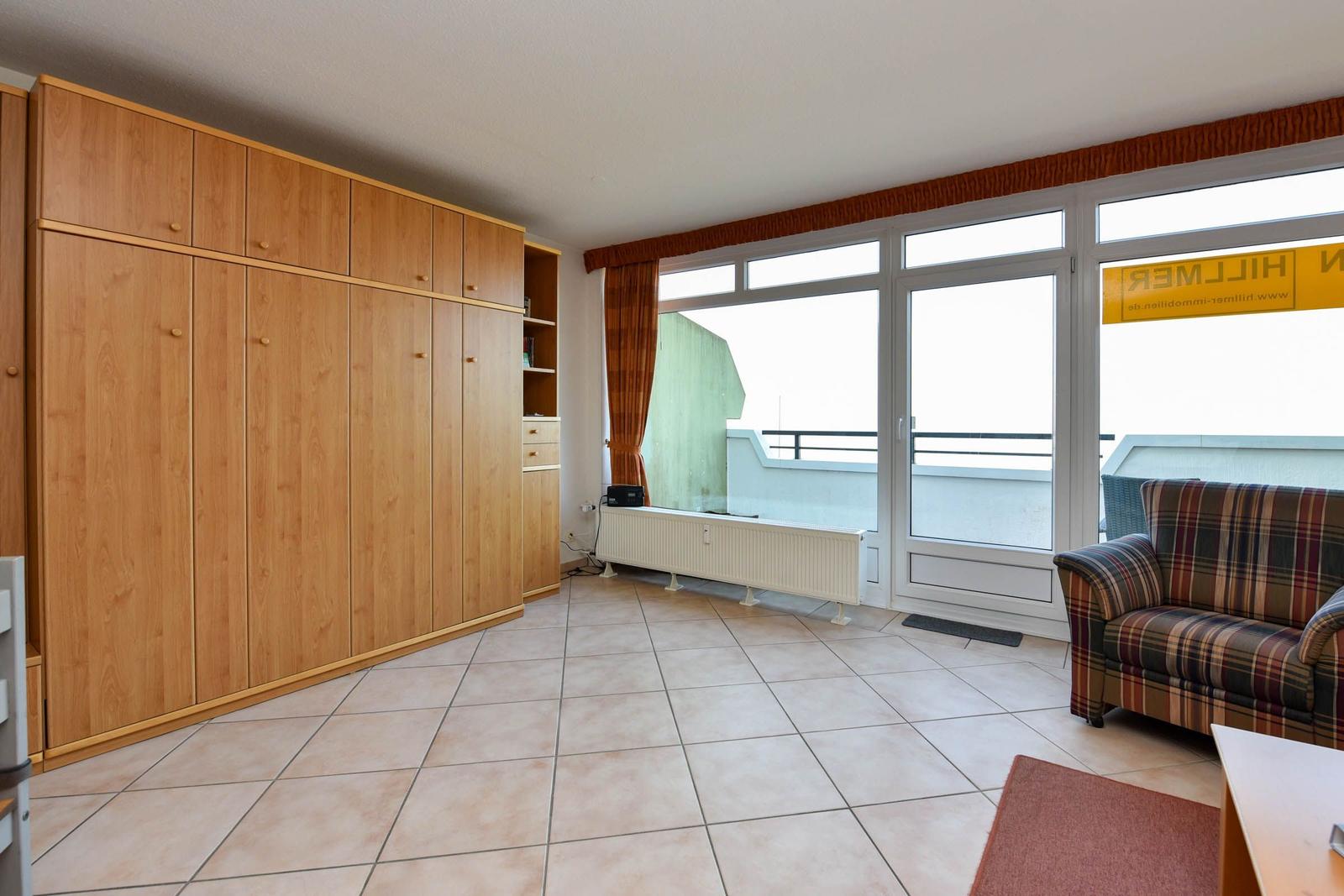 Großes Zimmer mit Holzschrank, Terrassentür und gemütlichem Sofa.