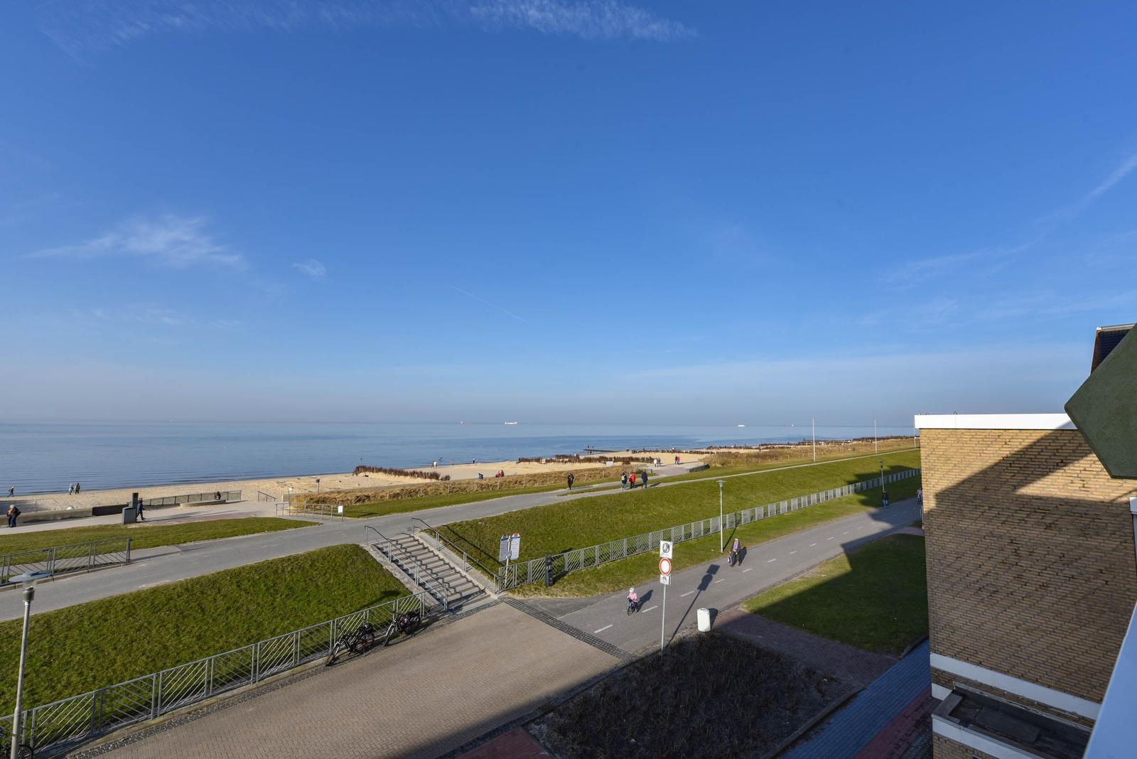 Panoramablick auf Strand, Grünflächen und Promenade unter blauem Himmel.
