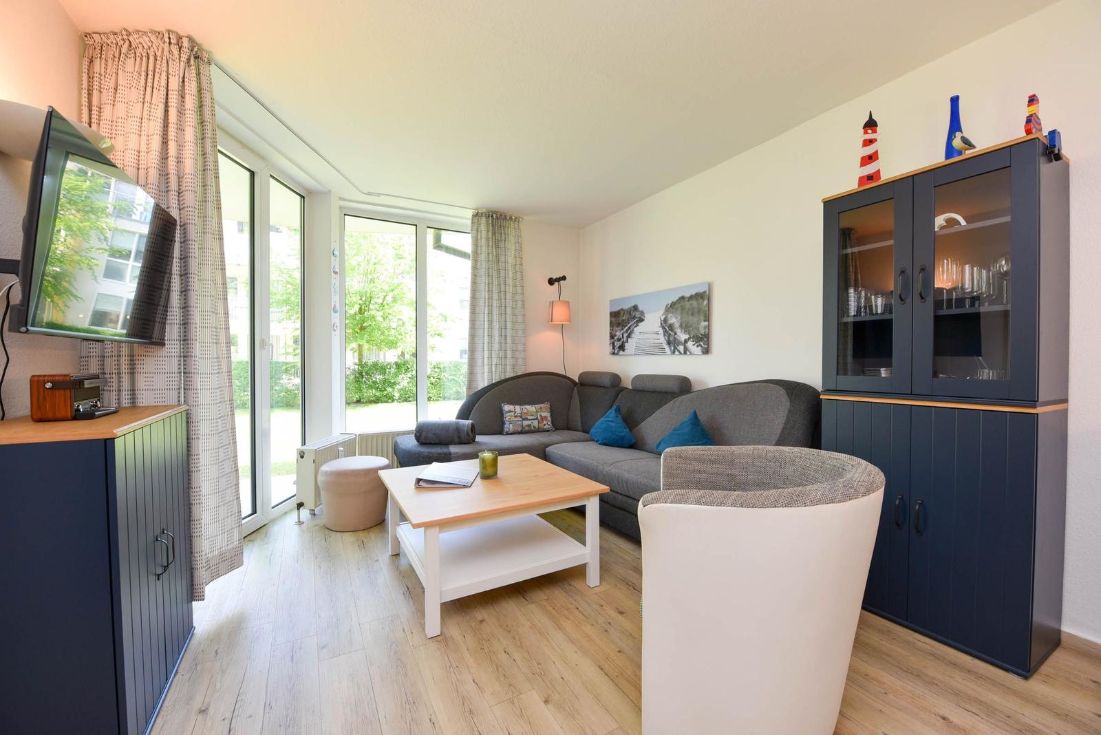 Wohnzimmer mit Sofa, Couchtisch und Glaswand-Schrank. Fenster zur Terrasse.