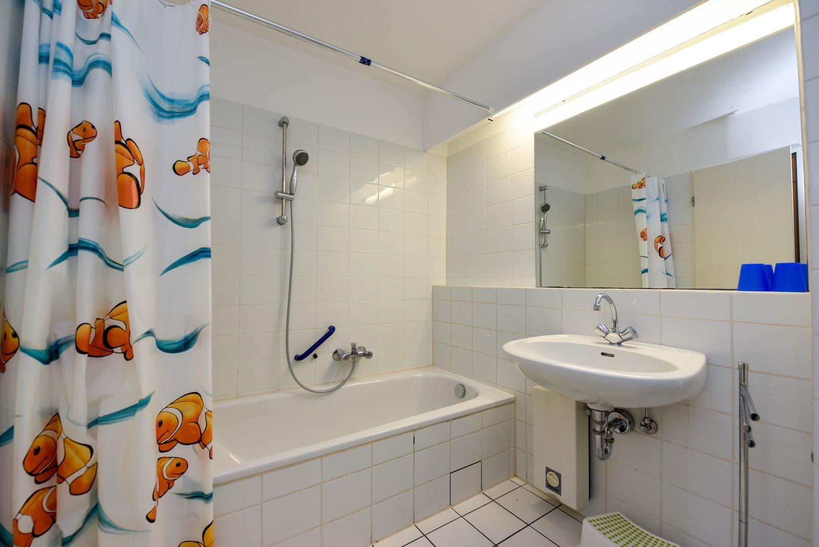 Badezimmer mit Badewanne, Dusche, Waschbecken und Spiegel mit Beleuchtung.