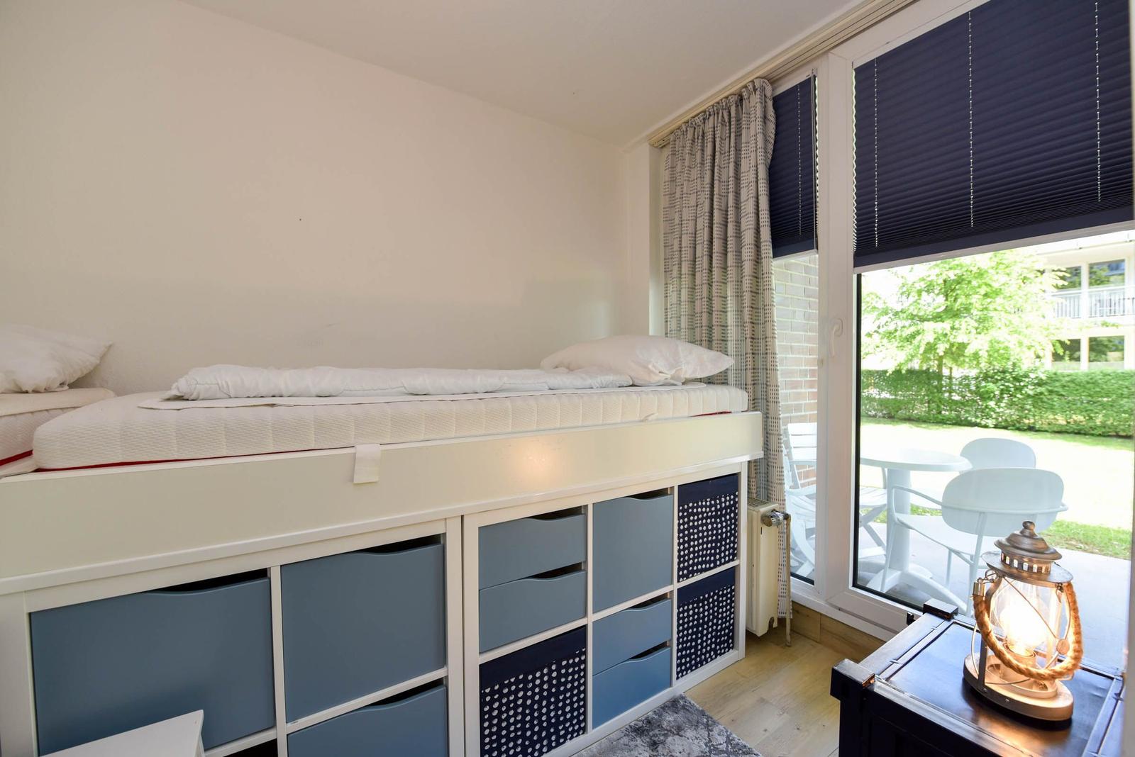Ein Schlafzimmer mit Hochbett und Stauraum unter dem Bett. Durchgang zum Balkon mit Tisch und Stühlen.