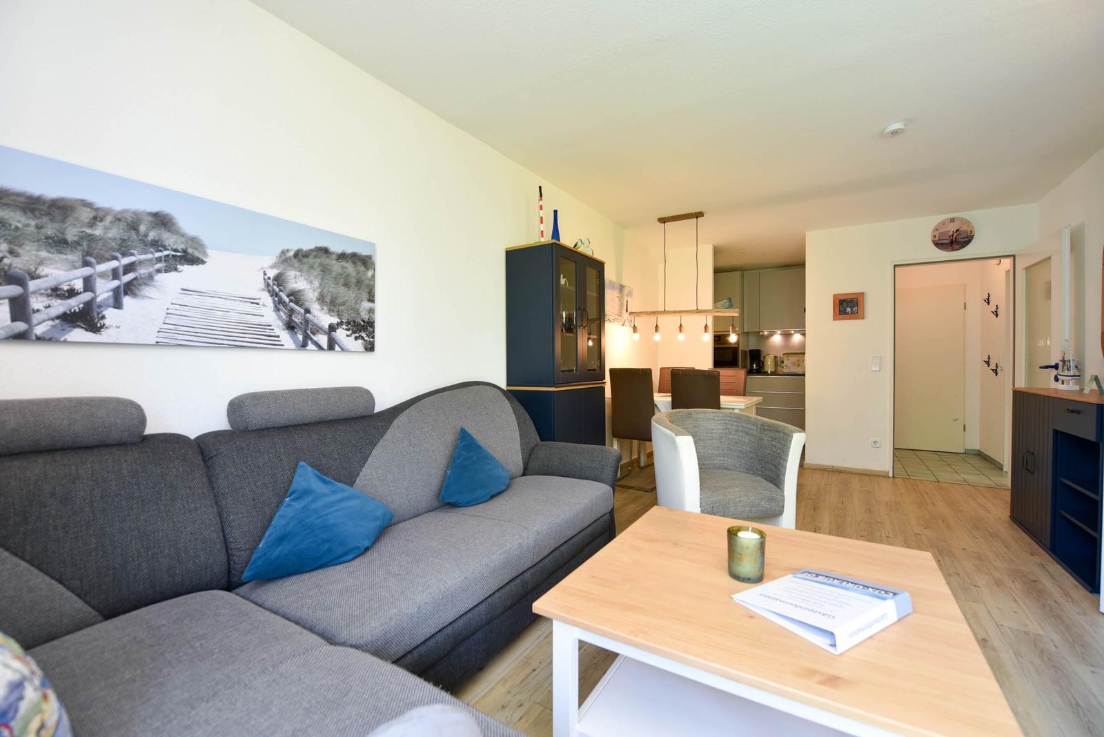 Wohnzimmer mit Sofa, Couchtisch und Wandbild. Küche und Essbereich im Hintergrund.