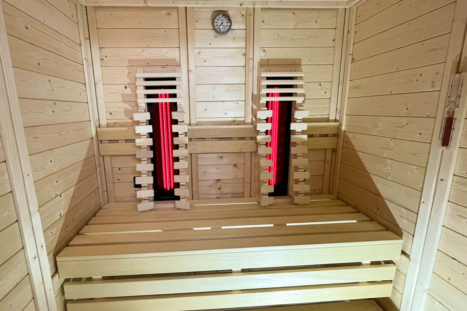 Sauna with wooden bench and red heating elements on the wall.