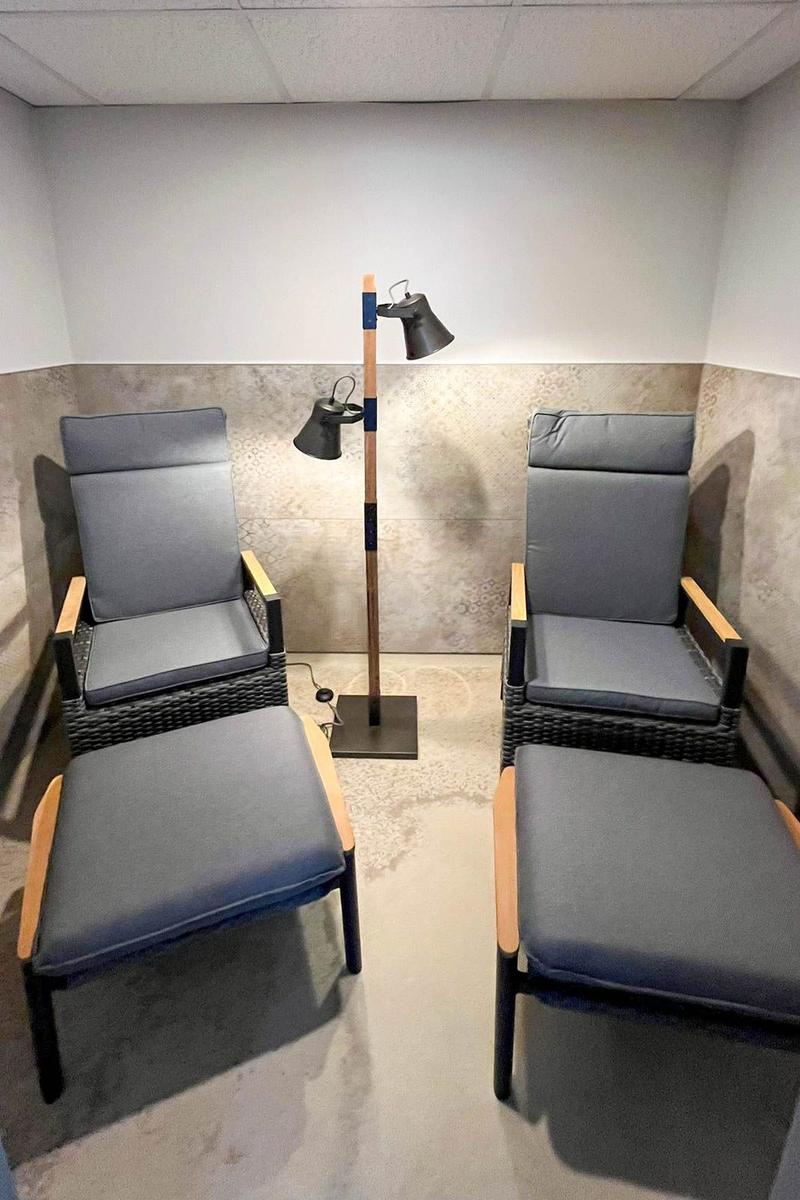 Two chairs with footstools and a floor lamp in a room with tiled walls.
