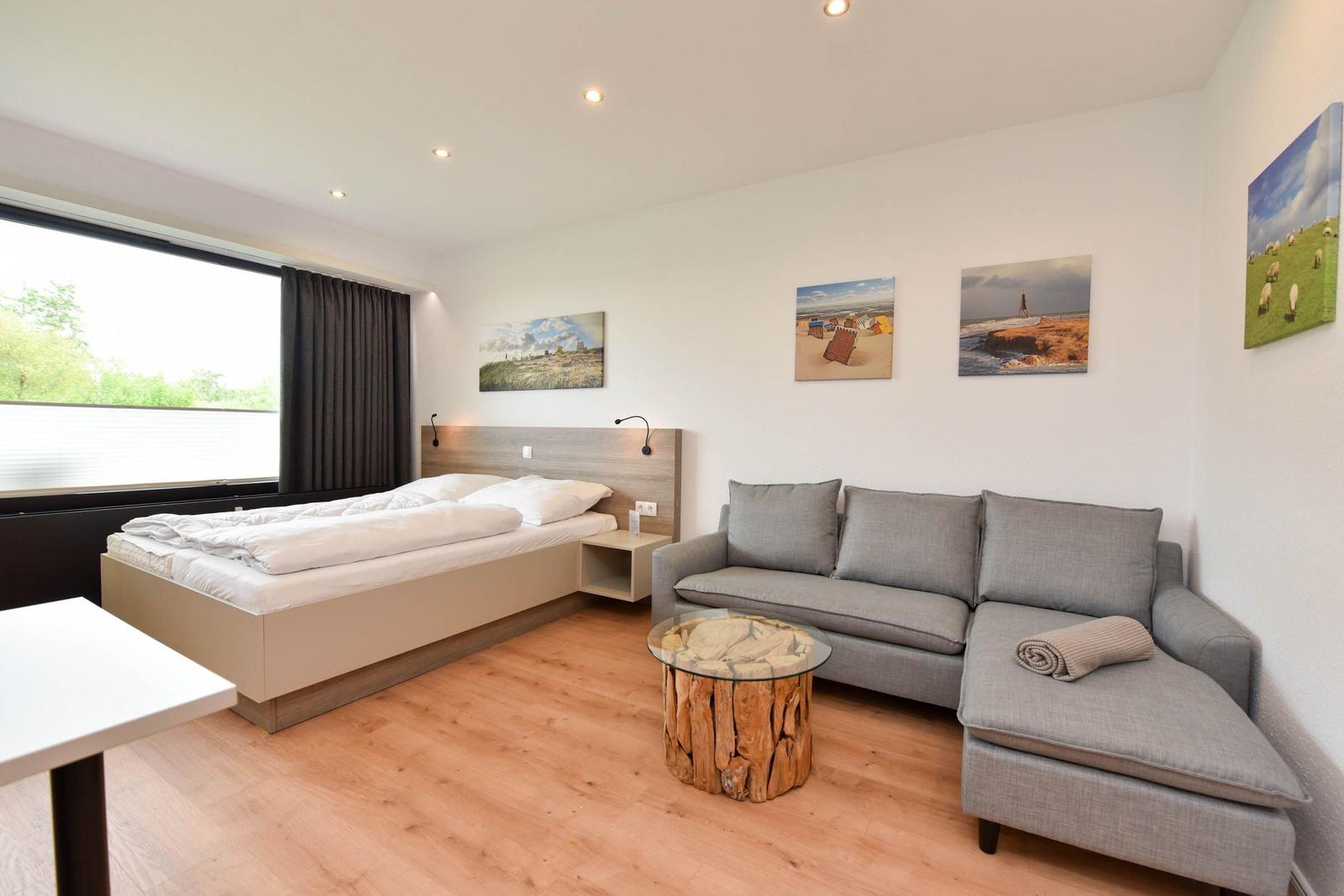 Ein Schlafzimmer mit Bett, Sofa und Holzboden. An der Wand hängen Bilder.
