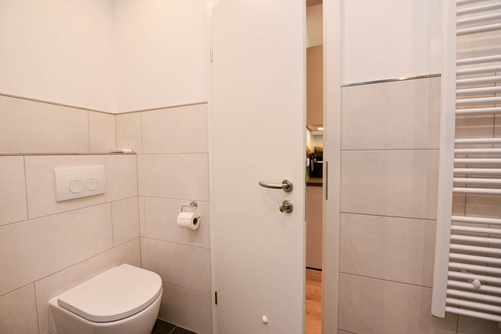 Toilettenbereich mit WC, Toilettenpapierhalter und Heizkörper an der Wand.