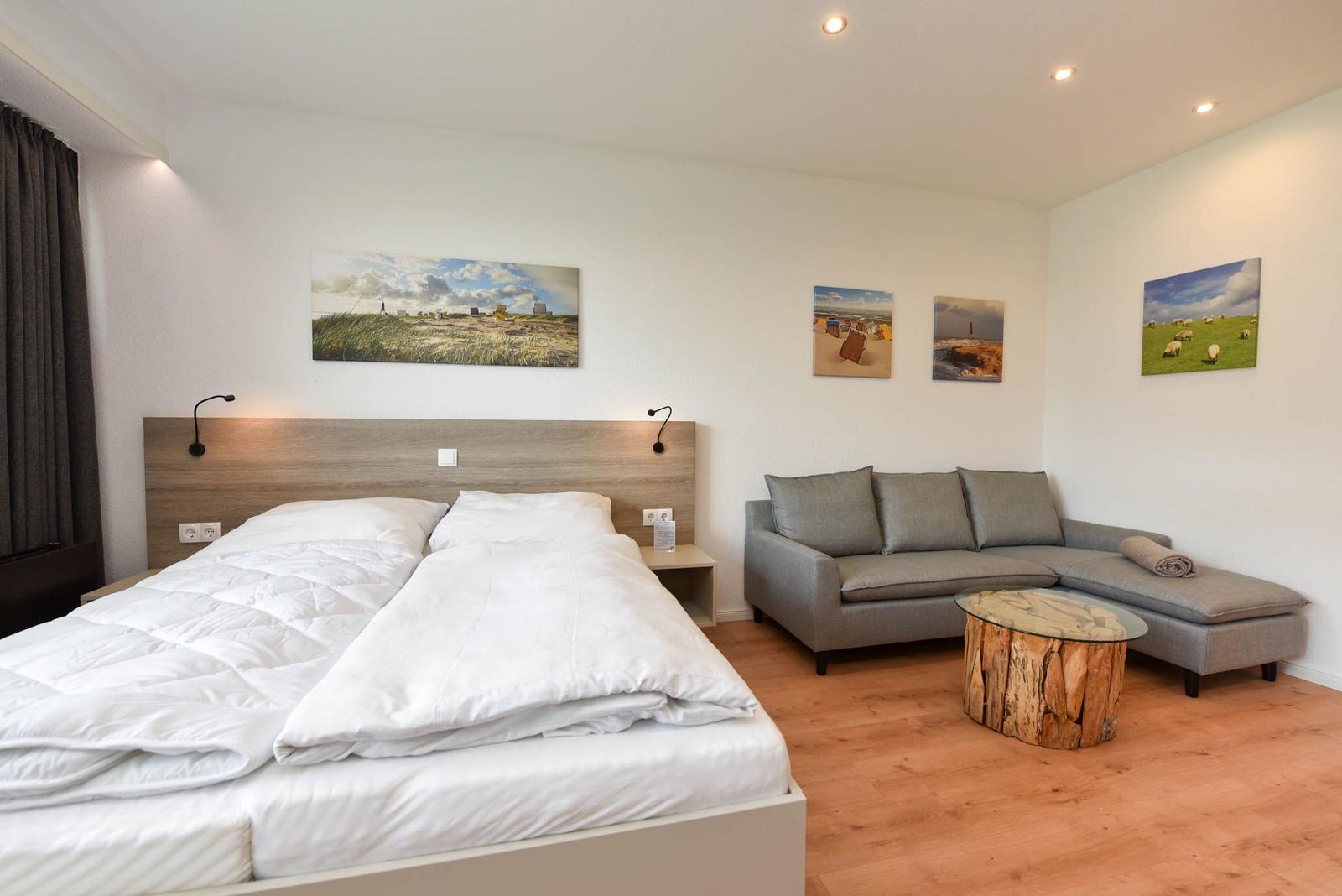 Schlafzimmer mit Doppelbett, Sofa und Wandbildern.