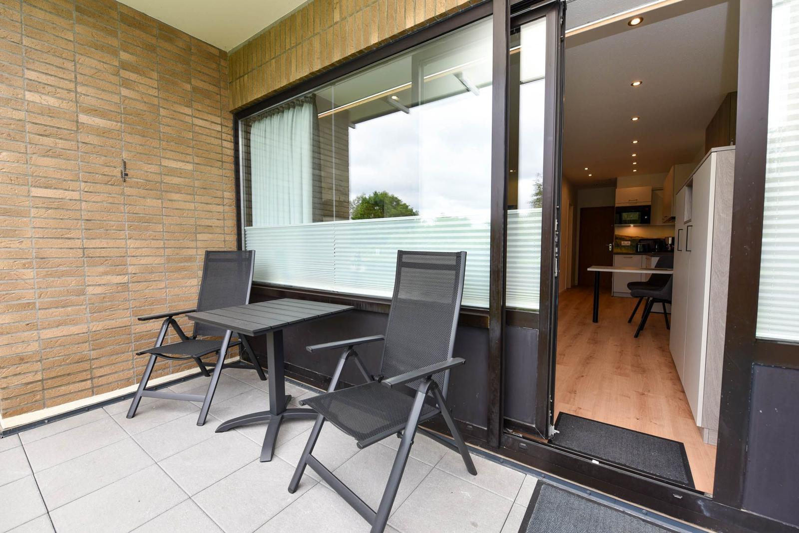 Terrasse mit Tisch und zwei Stühlen. Durch Glastür im Wohnbereich.