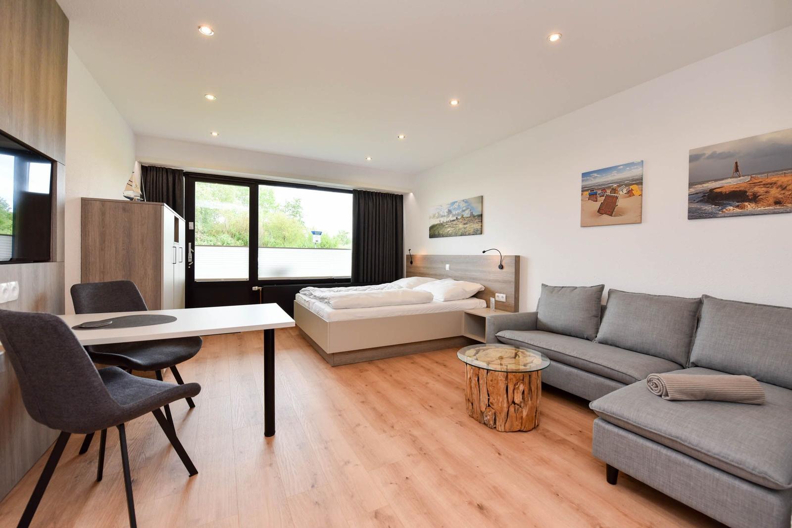 Ein Schlafzimmer mit Sofa, Tisch und Bett. Holzboden und Fenster mit Blick nach draußen.