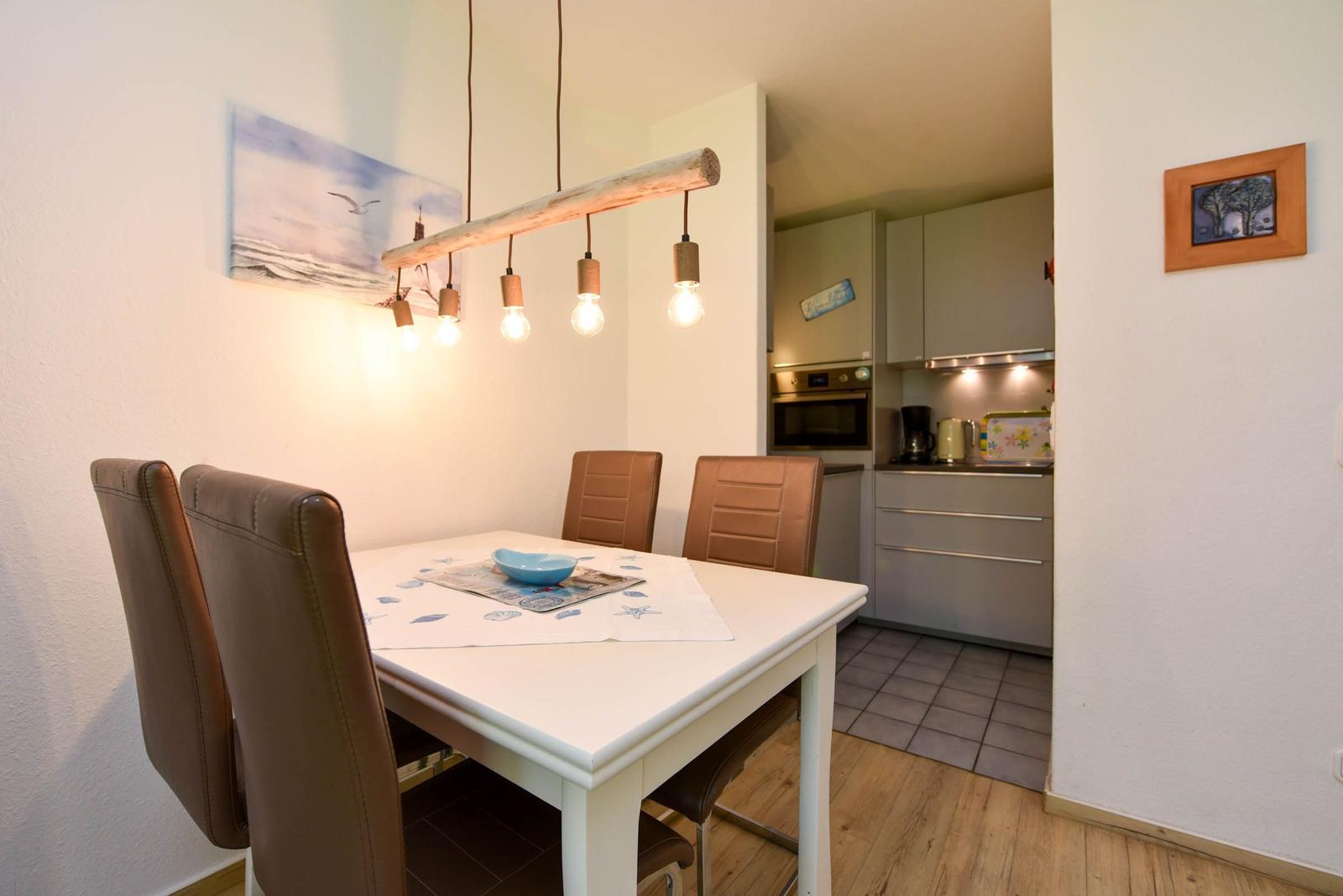 Esszimmer mit Tisch, Stühlen und Küchenbereich im Hintergrund.