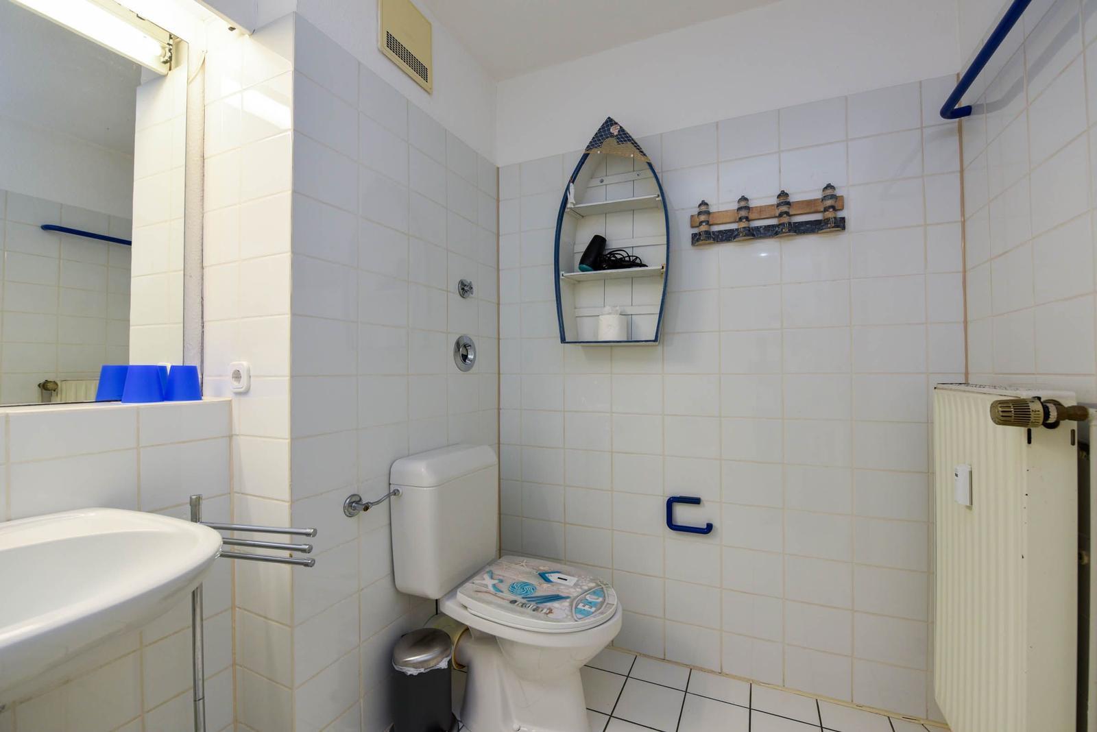 Badezimmer mit Toilette, Waschbecken und Duschbereich mit Bootsregal und Leuchtturm-Dekoration.