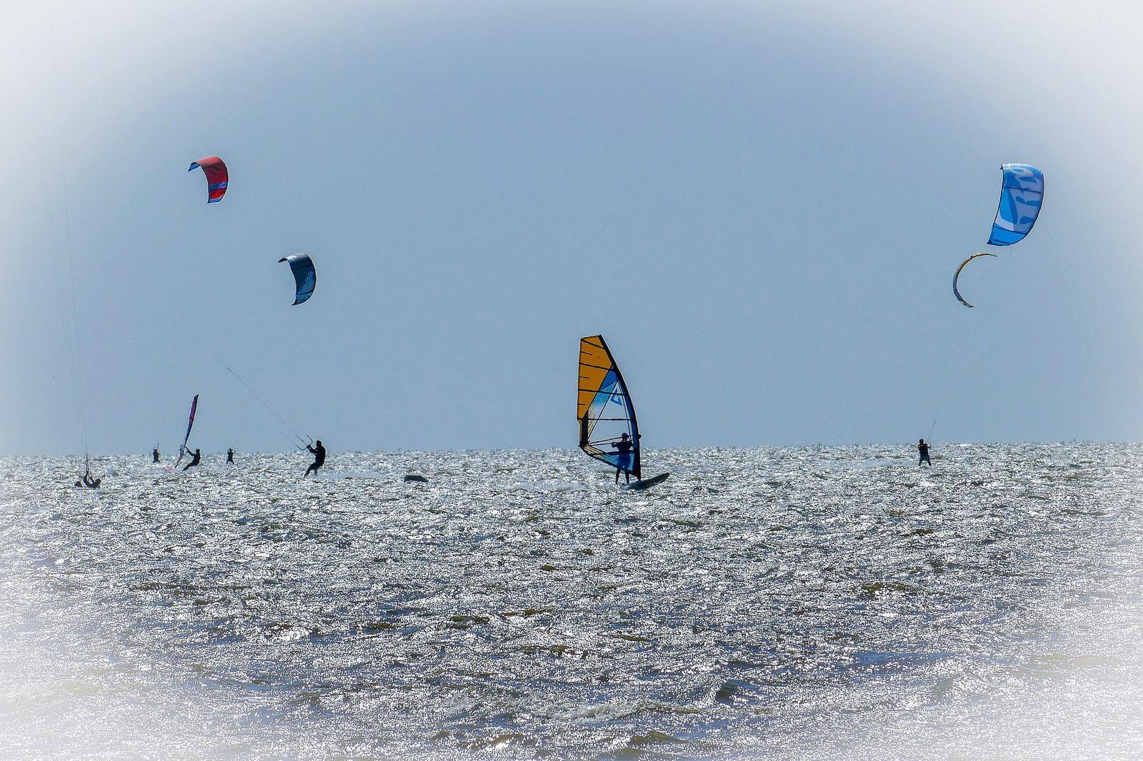Kitesurfers and windsurfers on the water under a clear sky.