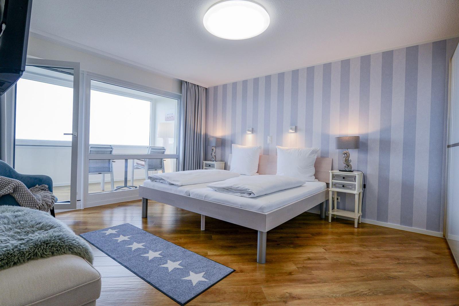 Bedroom with balcony, bed, nightstand, and hardwood floor.