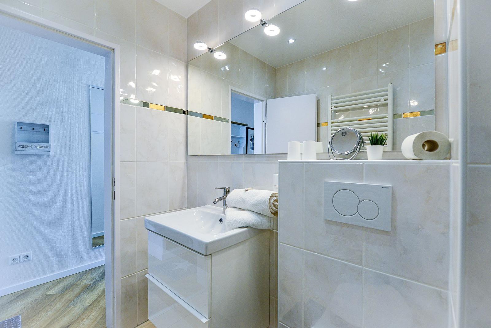 Bathroom with sink, mirror, and toilet. Tiled wall and wooden floor.