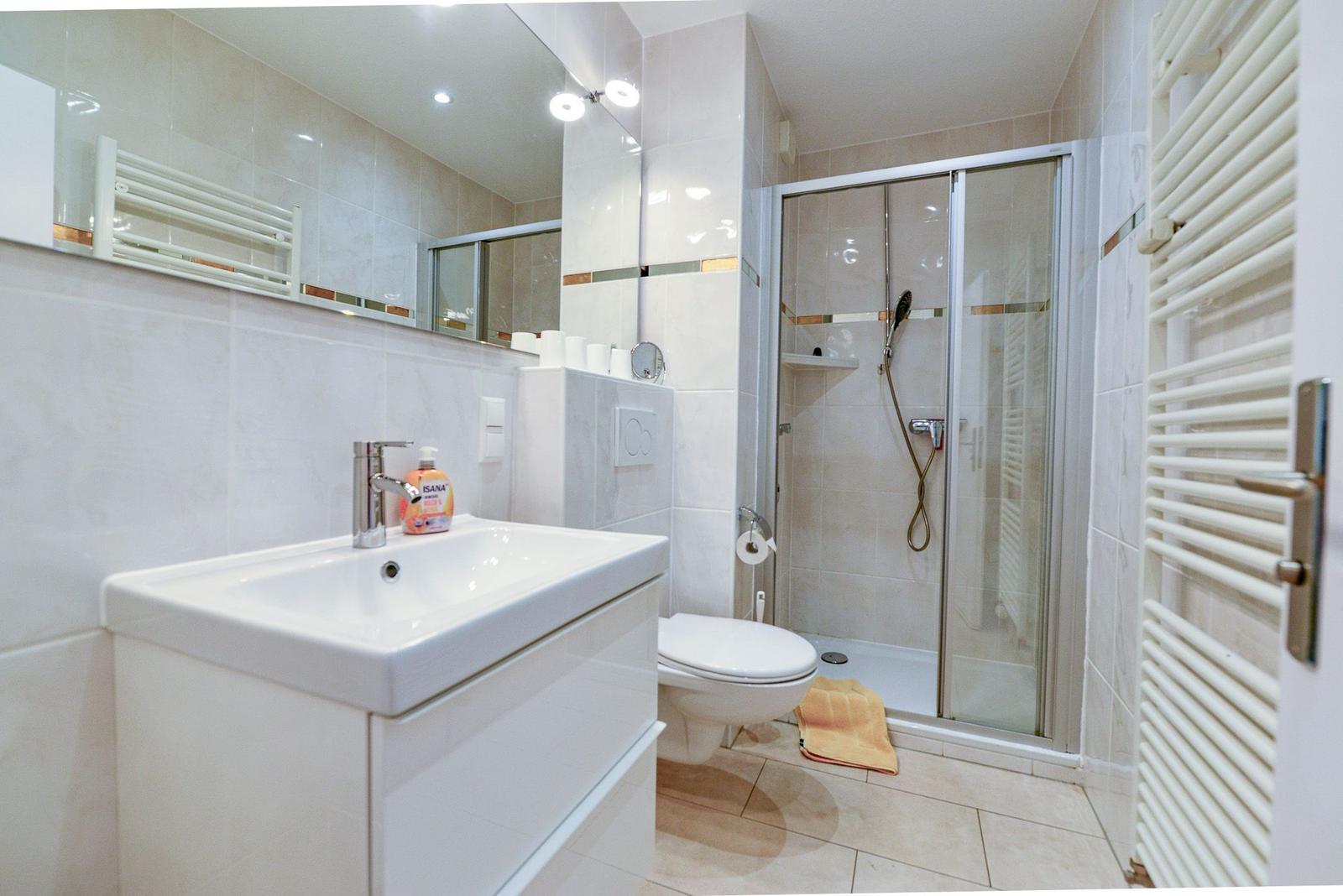 Bathroom with shower, sink, and toilet. White tiles and heater.