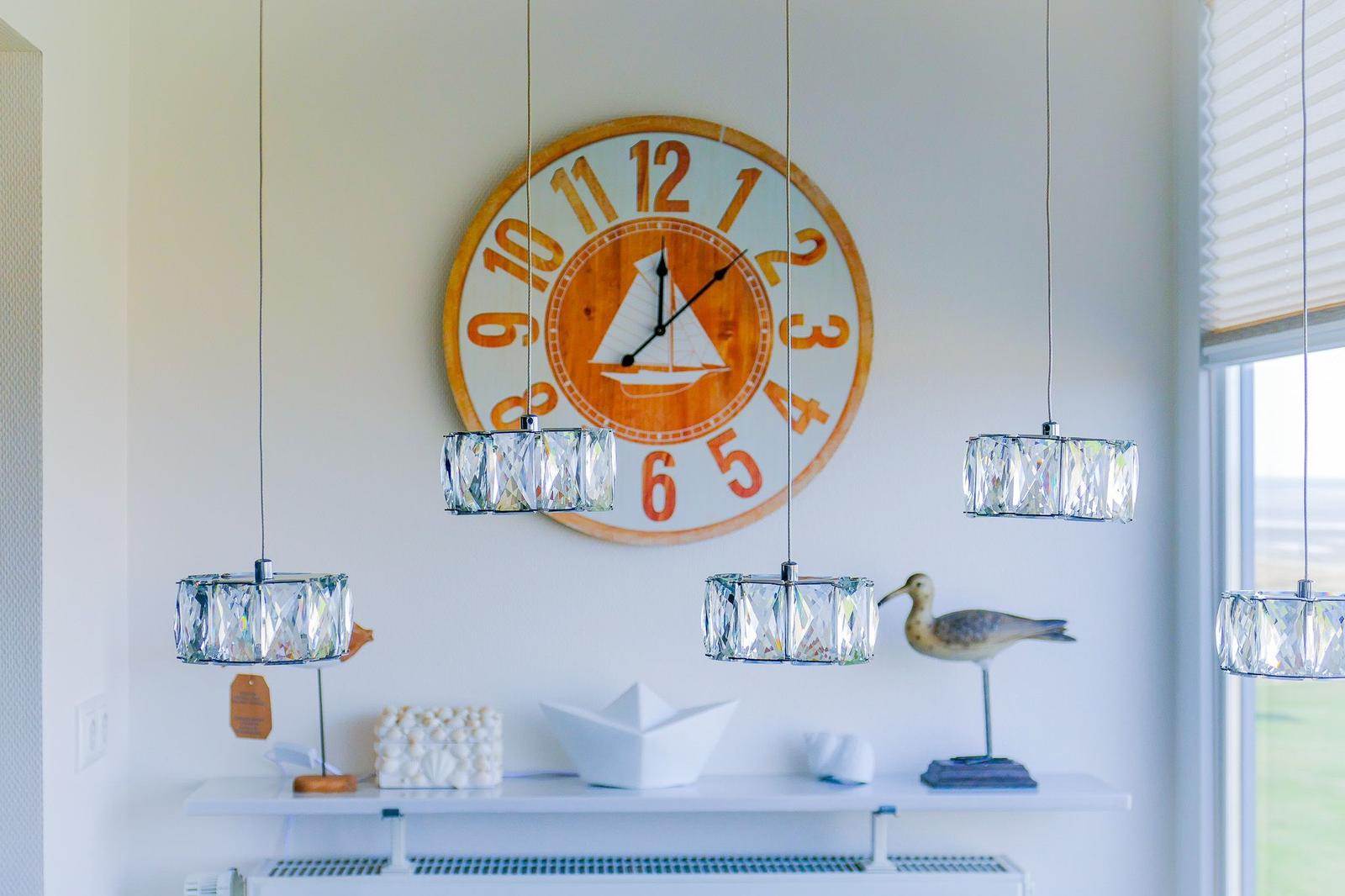 Wall clock with sailboat, three pendant lights, and decorative items on a shelf.