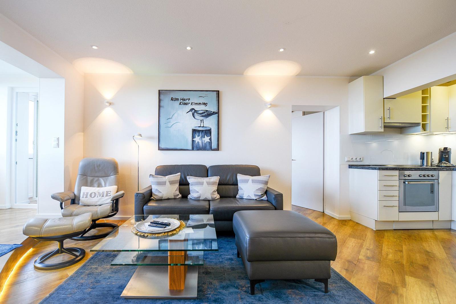 Living room with sofa, armchair, and kitchen area. Wall art with bird motif.