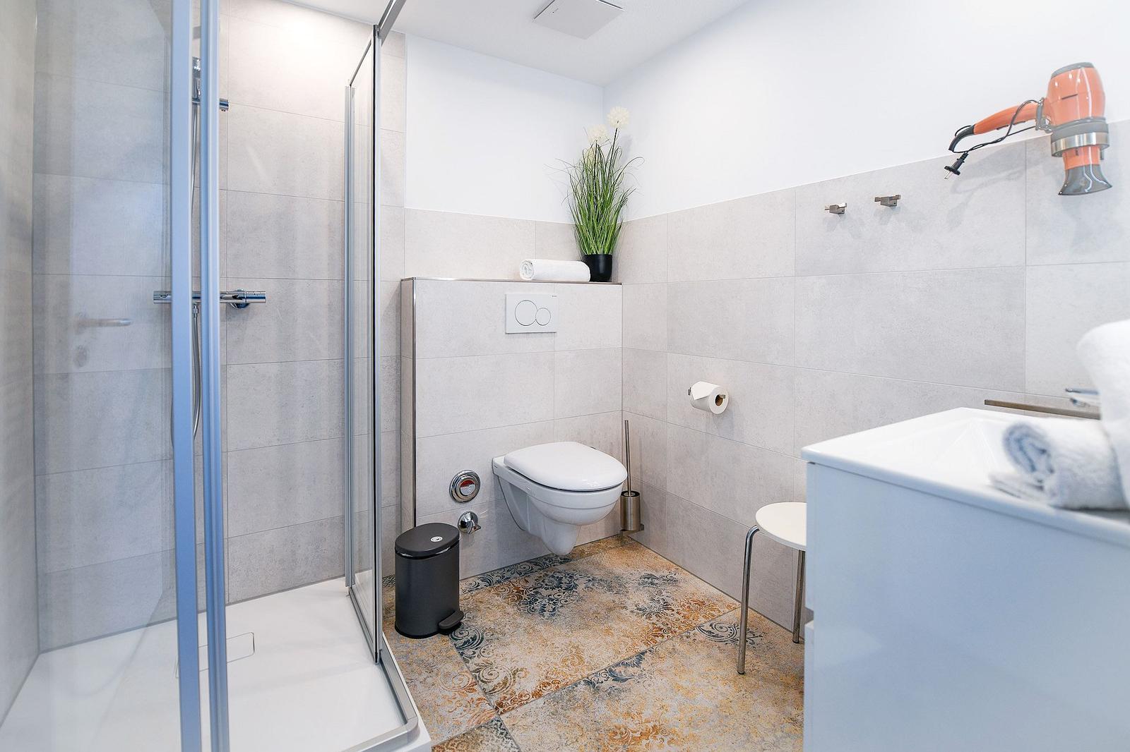 Badezimmer mit Dusche, Toilette und Waschbecken. Orange Haartrockner an der Wand.