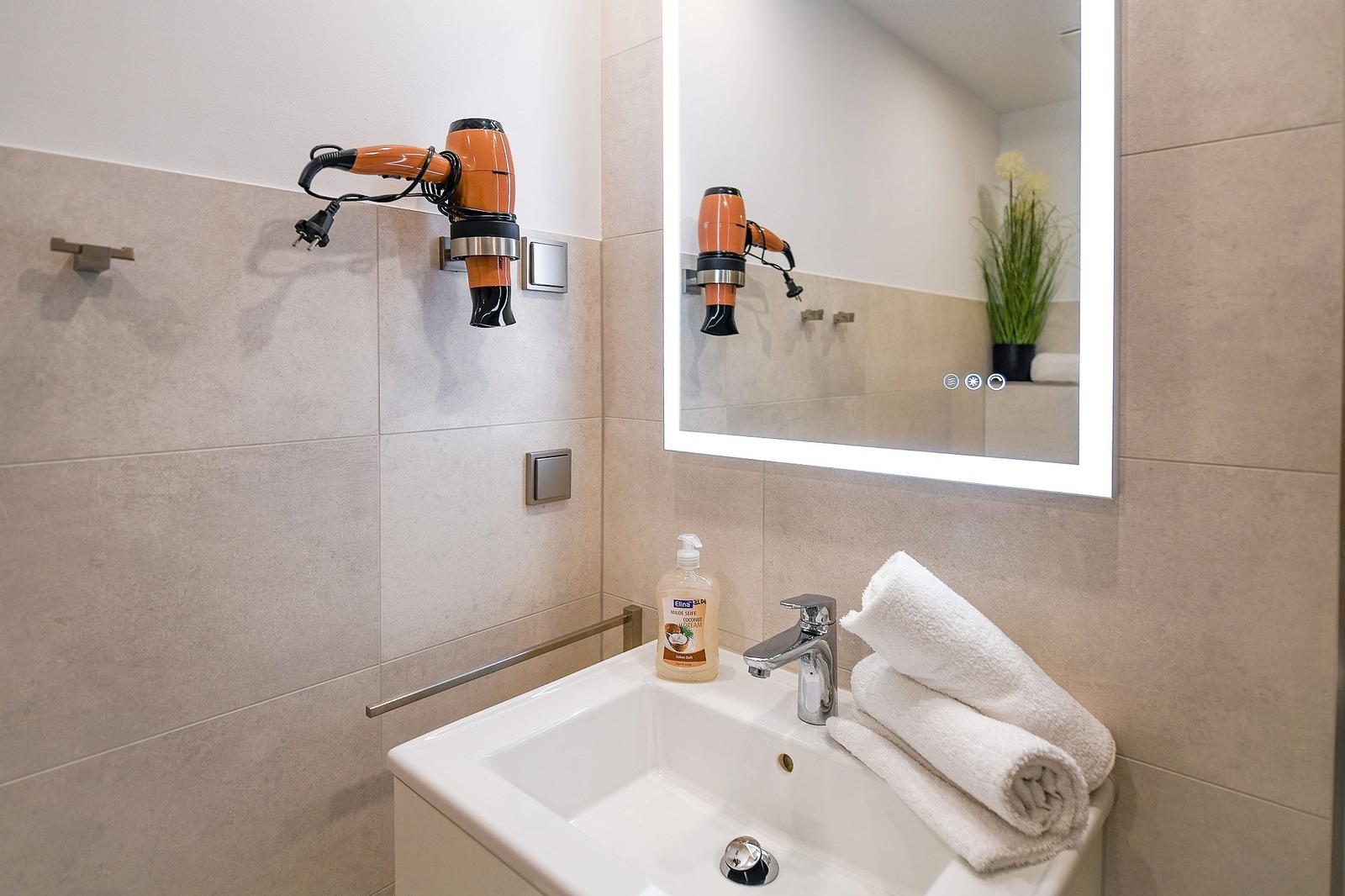 Badezimmer mit Spiegel, Handtuch und Haartrockner an der Wand.