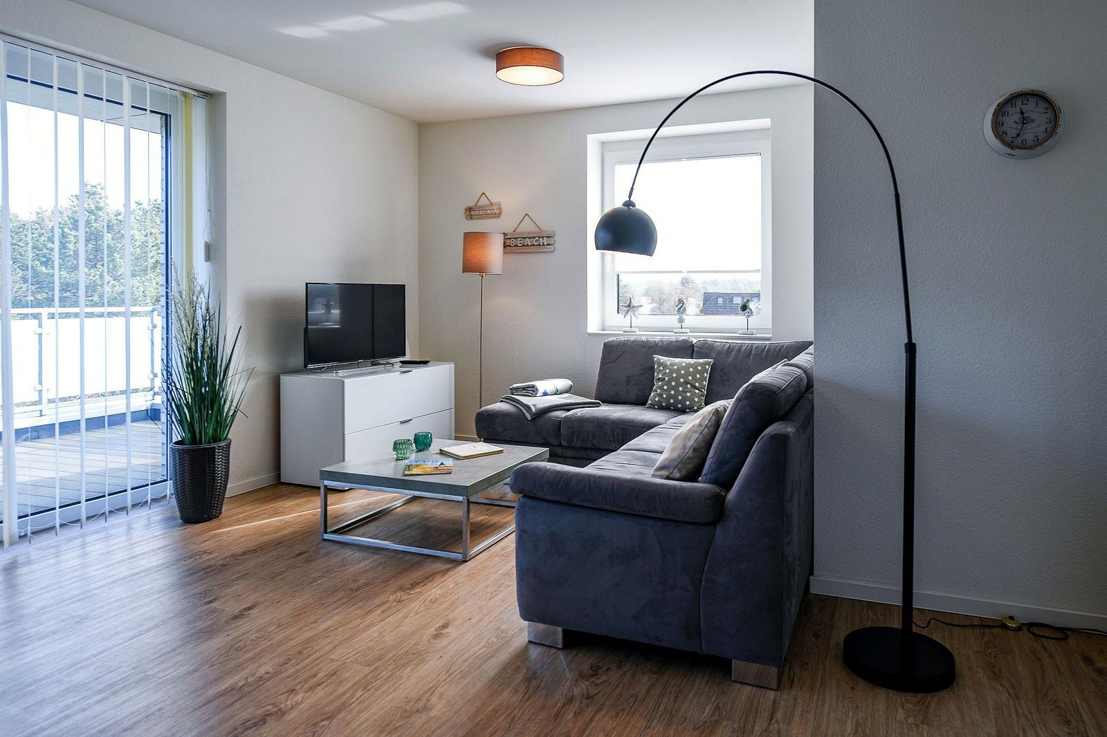 Wohnzimmer mit Sofa, Couchtisch und Fernseher. Durchgang zur Terrasse mit Blick auf Grün.