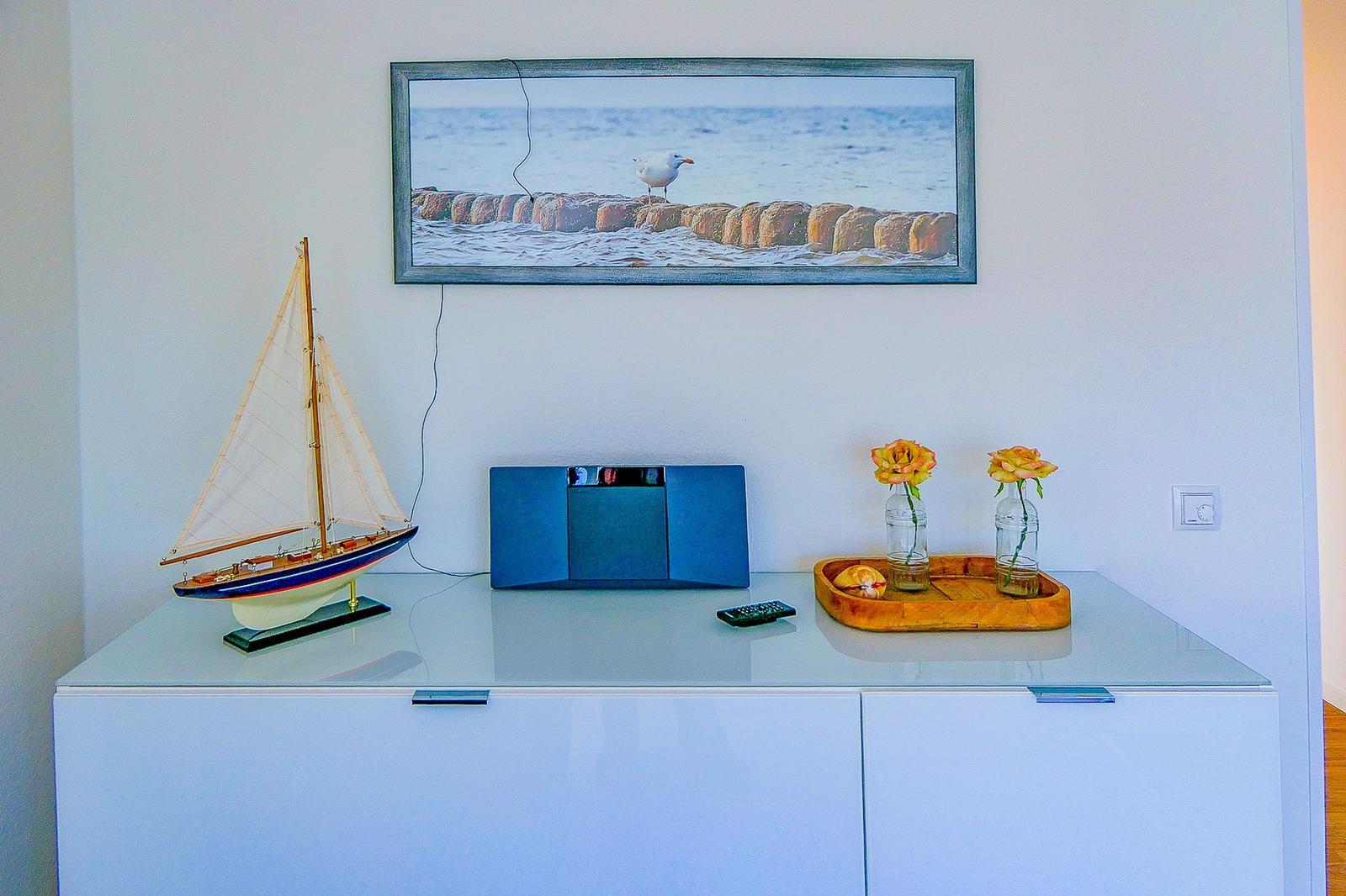 Auf einem Schrank steht ein Segelbootmodell, ein Radio und zwei Rosen in Gläsern.