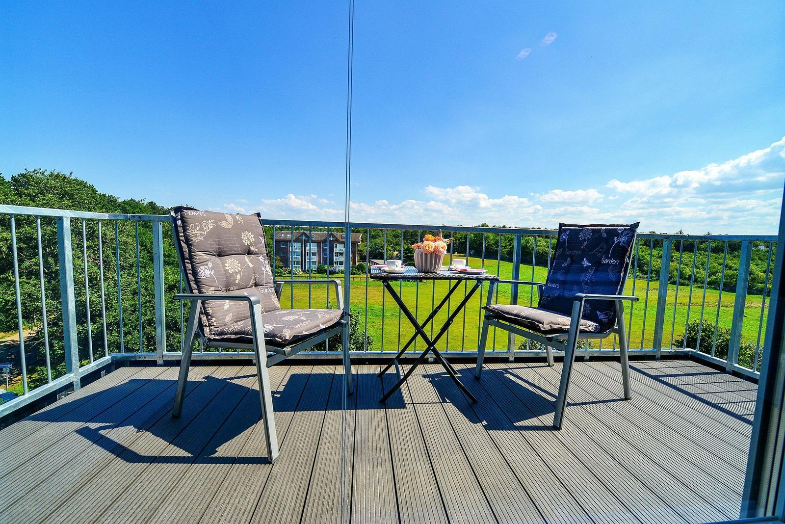 Terrasse mit zwei Stühlen und Tisch. Blick auf grünes Feld und Himmel.