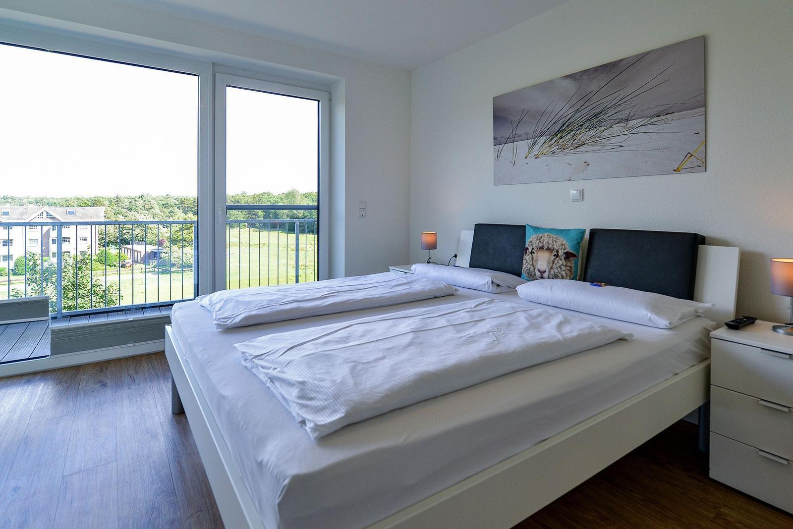 Schlafzimmer mit Doppelbett, Balkon und Wandbild. Holzfußboden und Nachttische.