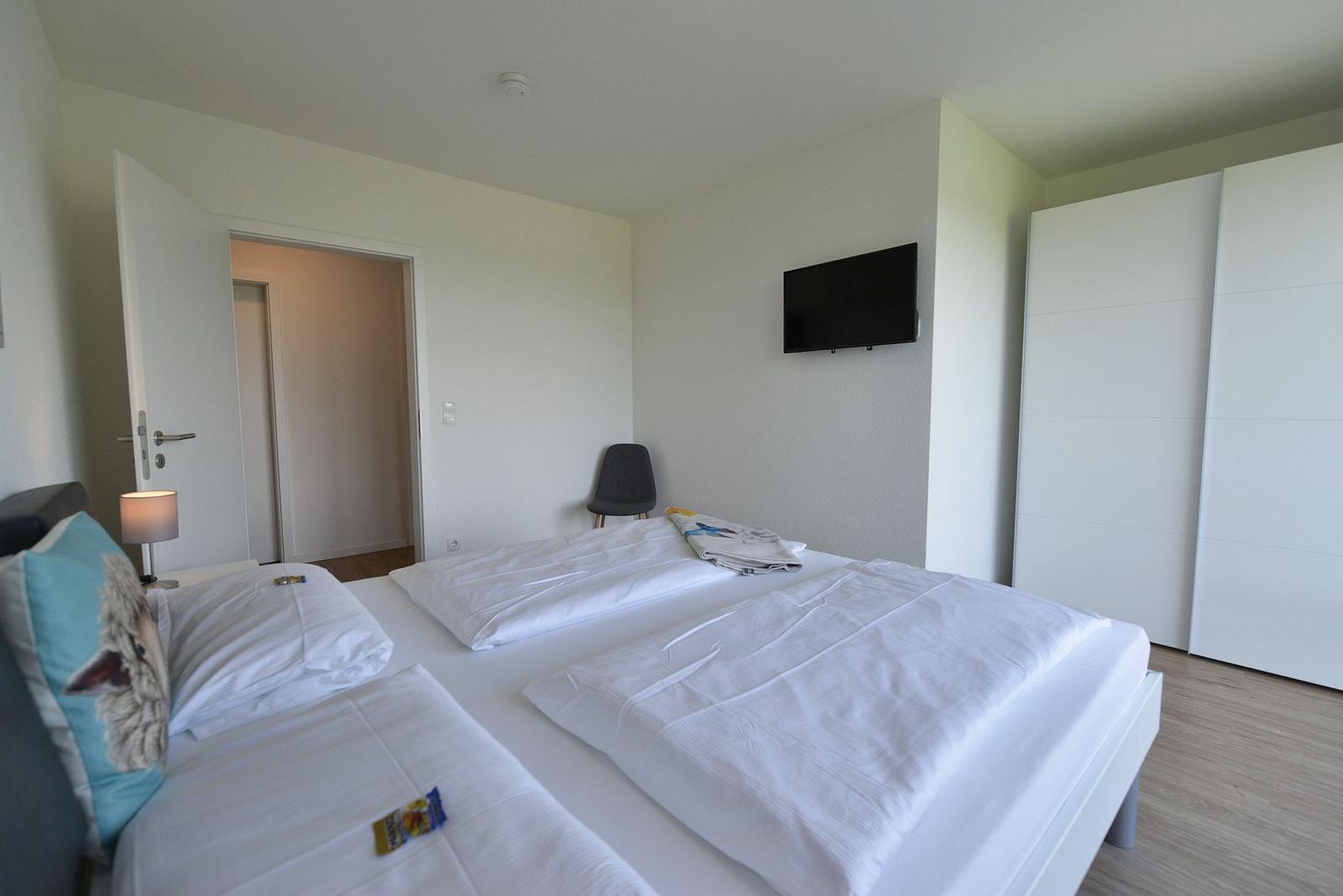 Schlafzimmer mit Doppelbett, Fernseher und Kleiderschrank.