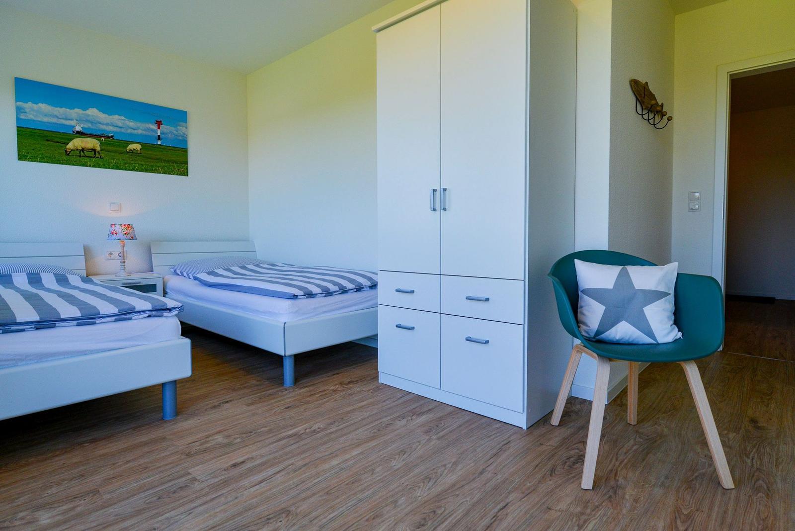 Zwei Betten, Kleiderschrank und Sessel mit Kissen im Schlafzimmer.