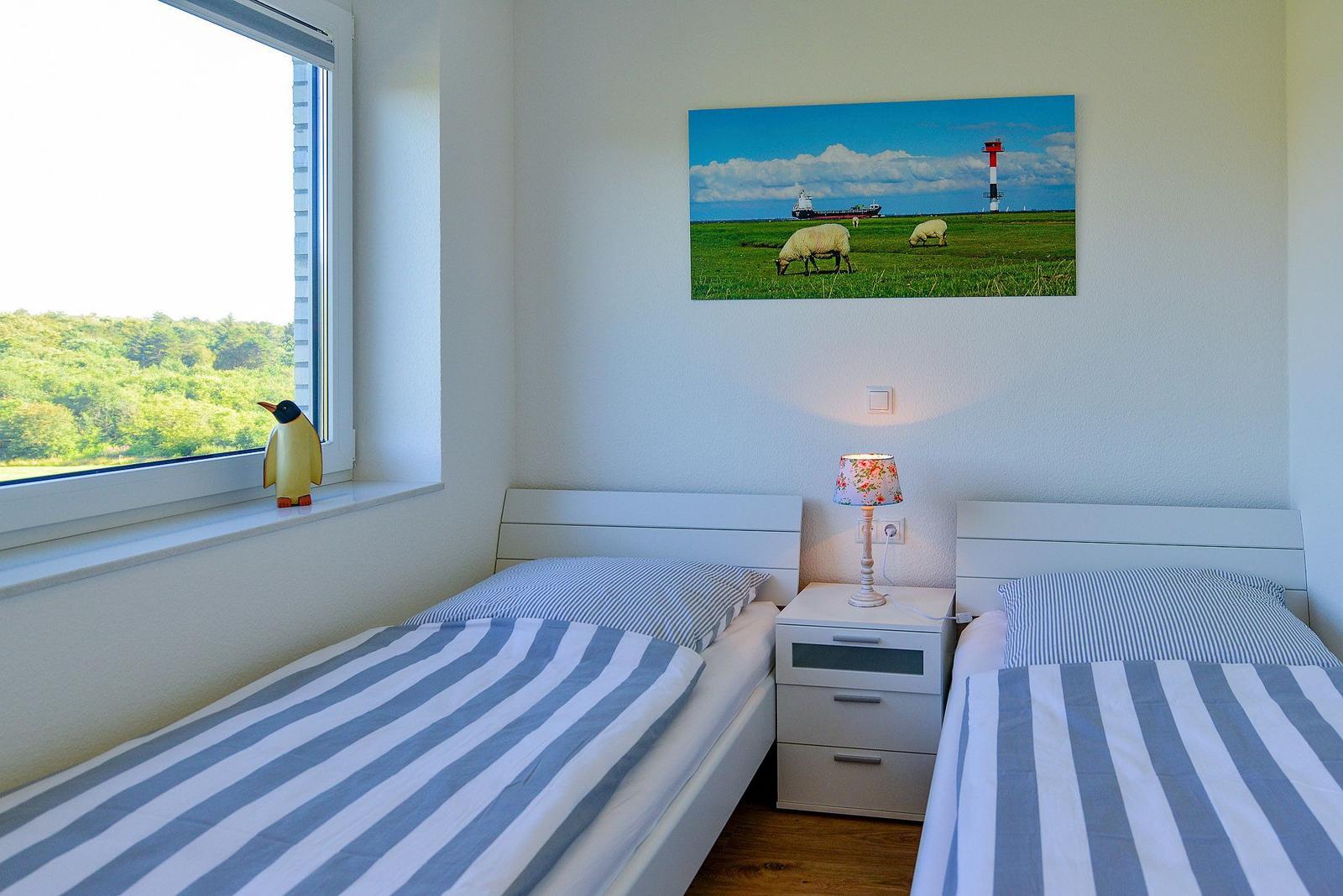 Zwei Betten mit gestreiften Bettwäsche, Nachttisch und Wandbild mit Leuchtturm.
